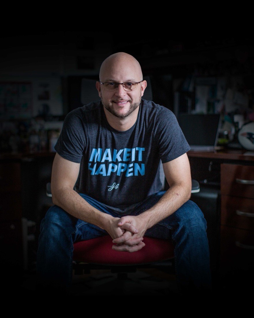 John Barrows seated in his office wearing a Make It Happen shirt